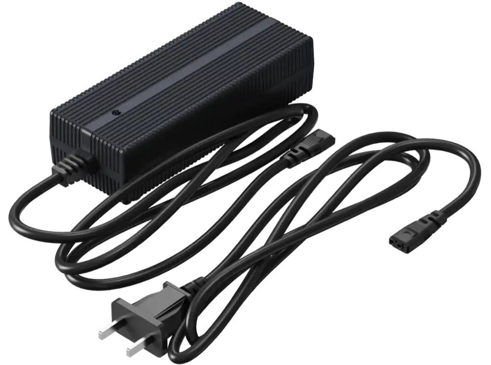 Ładowarka UNITREE Go2 Fast Charge Zdjęcie studyjne, przedstawiające czarną ładowarkę sieciową (zasilacz) do robota Unitree. Zasilacz ma żeberkowaną obudowę. Widoczne są dwa kable: jeden z wtyczką IEC C5 (koniczynka) do podłączenia do zasilacza, a drugi z wtyczką typu E/F (europejska) do gniazdka.