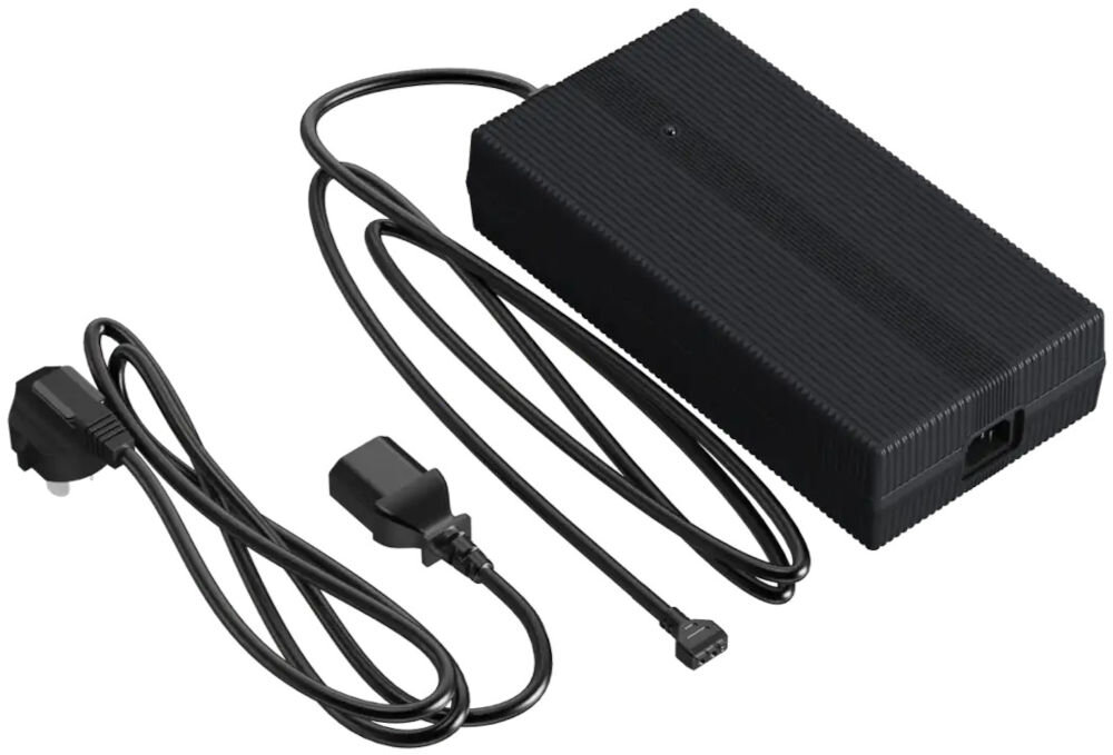 Ładowarka UNITREE Go2 Fast Charge Zdjęcie studyjne, przedstawiające czarną, prostokątną ładowarkę sieciową do robota Unitree. Obok zasilacza leży dołączony, zwinięty kabel zasilający z wtyczką typu G (UK/Irlandia) oraz drugi, mniejszy kabel zasilający.