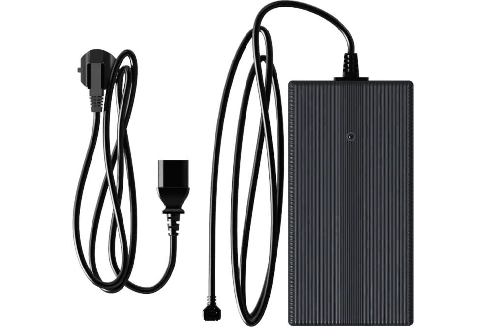 Ładowarka UNITREE Go2 Fast Charge Zdjęcie studyjne, przedstawiające czarną, prostokątną ładowarkę sieciową (zasilacz) do robota Unitree, ułożoną pionowo. Widoczny jest długi, czarny kabel z wtyczką do robota oraz dołączony, zwinięty kabel zasilający z wtyczką typu G (UK/Irlandia).