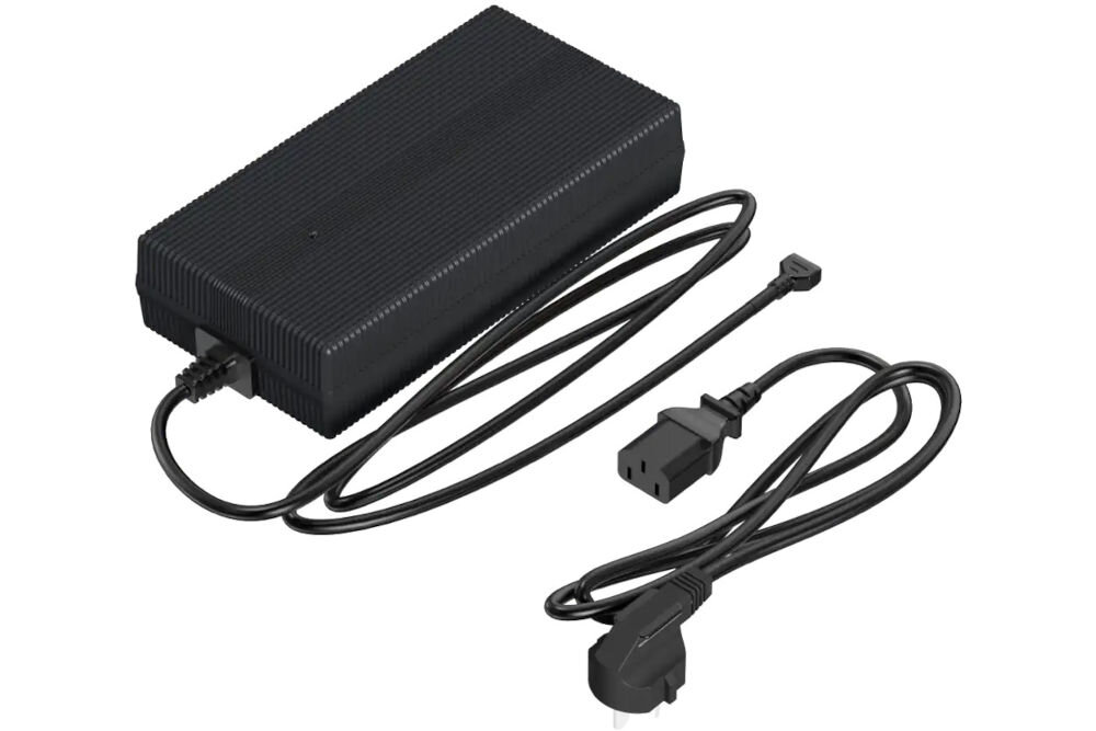 Ładowarka UNITREE Go2 Fast Charge Zdjęcie studyjne, przedstawiające czarną ładowarkę sieciową (zasilacz) do robota Unitree. Zasilacz ma żeberkowaną obudowę. Widoczne są dwa kable: jeden z wtyczką IEC C5 (koniczynka) do podłączenia do zasilacza, a drugi z wtyczką typu E/F (europejska) do gniazdka.