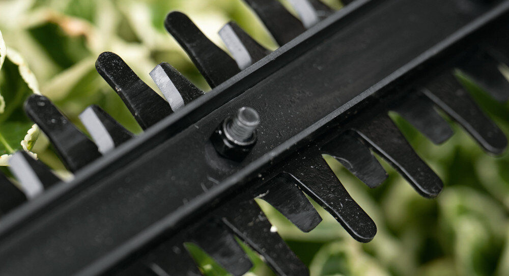 Nożyce do żywopłotu BOSCH EasyHedgeCut 18V-44-11 zbliżenie na ostrza w tle liście długość ostrza wynosi 52 cm odstępy między nożami 15 mm prędkość skokowa do 2400 min⁻¹ precyzyjne cięcie równomierny kształt żywopłotu