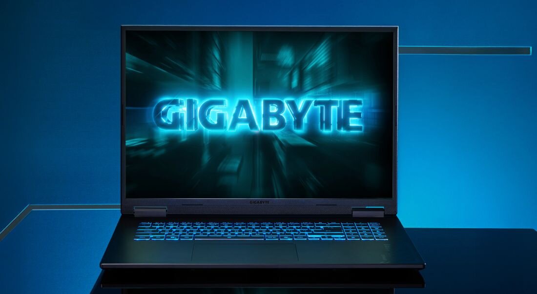 Laptop z wyświetlaczem pokazującym logo \'GIGABYTE\' na tle niebieskiego, futurystycznego wzoru. Klawiatura jest podświetlona na niebiesko.
