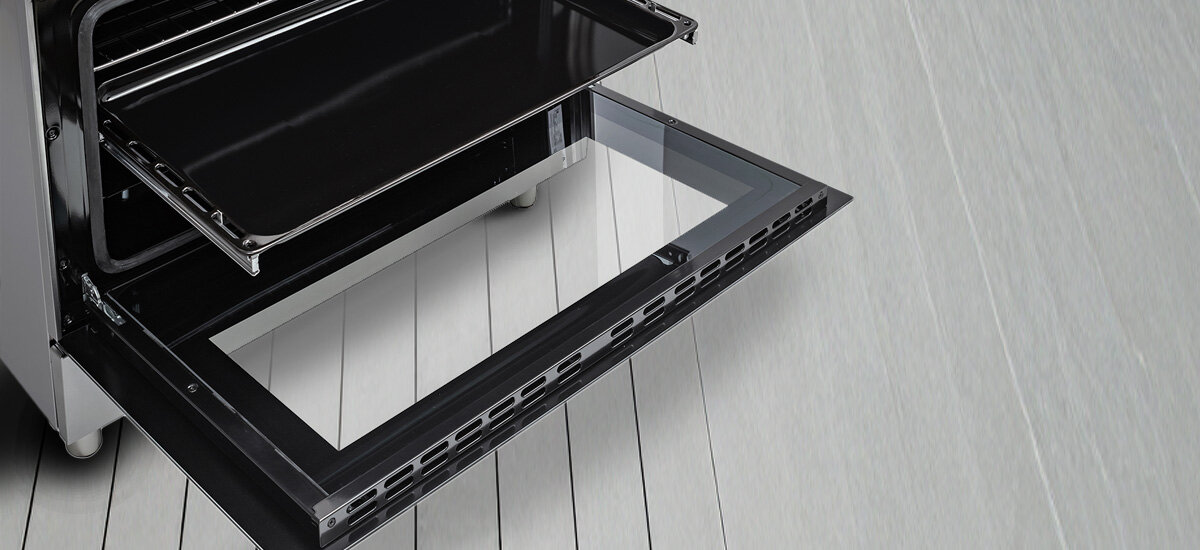 KUCHNIA DAEWOO F96CGDTE19INM-EE Zdjęcie przedstawia otwarty piekarnik kuchni wolnostojącej z uchyloną szklaną drzwiową i wysuniętą czarną blachą do pieczenia. Zdjęcie przedstawia także fragment metalowych prowadnic wewnątrz piekarnika oraz jasną podłogę z paneli lub płytek pod urządzeniem teleskopowa prowadnica piekarnik wysuwana blacha bezpieczeństwo użytkowania wygoda