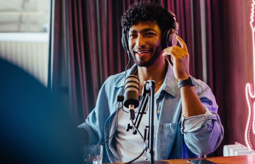 Karta graficzna ACER Nitro Intel Arc B570 OC 10GB Uśmiechnięty mężczyzna w słuchawkach i dżinsowej koszuli siedzi przed mikrofonem w studiu nagraniowym, multimedia, twórcy, zastosowanie