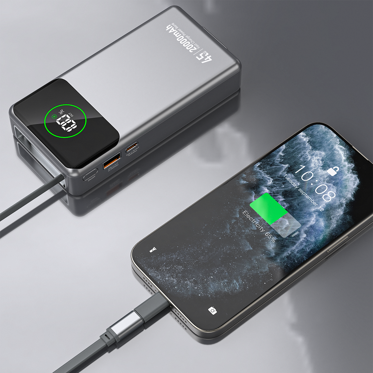 Na obrazie widać szary powerbank z wyświetlaczem pokazującym \'45W 20000mAh\' oraz podłączony do niego smartfon z ekranem pokazującym ładujący się poziom baterii na 65%.