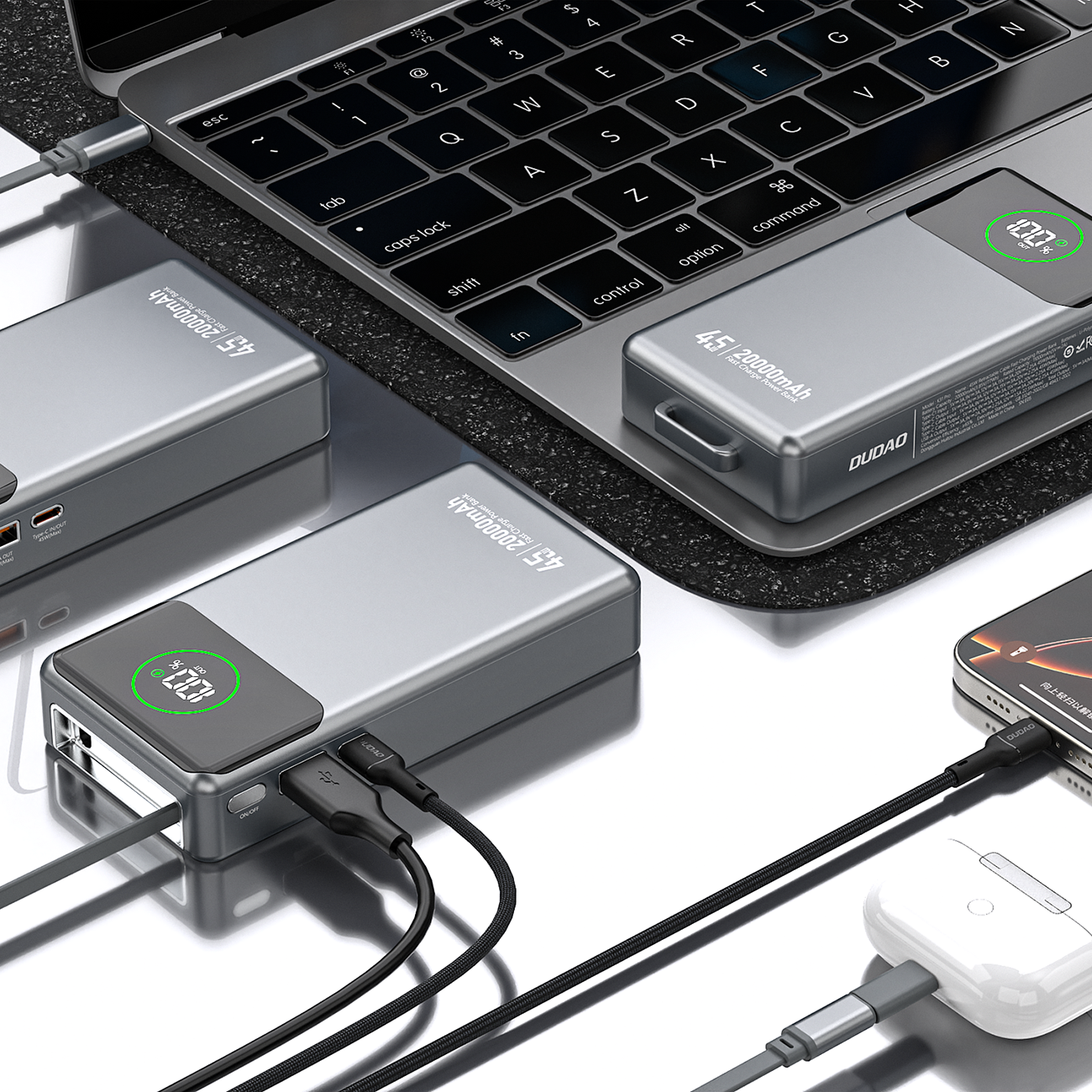 Na obrazie widoczne są szare powerbanki z napisem \'45W 20000mAh\' oraz logo \'DUDAO\', podłączone do różnych urządzeń elektronicznych. Powerbanki mają wyświetlacze pokazujące poziom naładowania baterii.