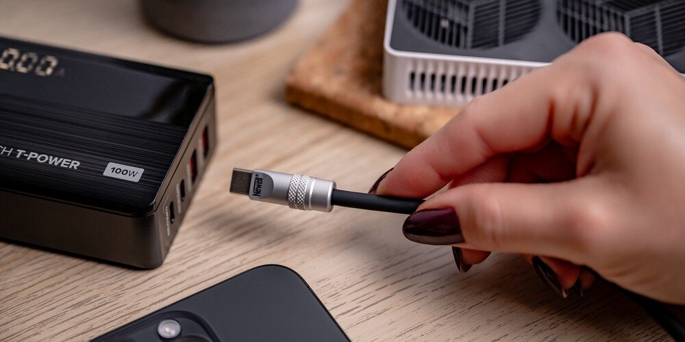 Kobieca dłoń wpina silikonowy kabel Newell USB-C do USB-C do leżącej na drewnianym blacie ładowarki.