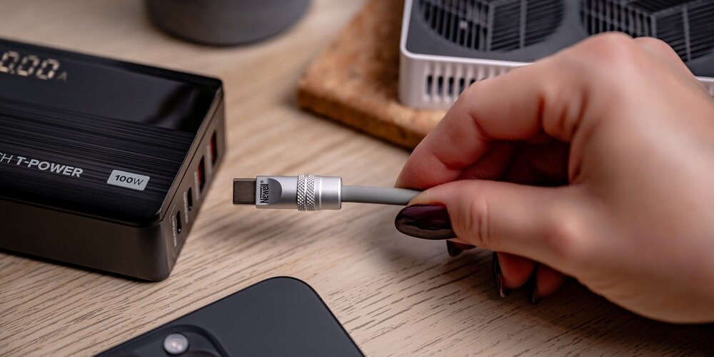 Kobieca dłoń wpina silikonowy kabel Newell USB-C do USB-C do leżącej na drewnianym blacie ładowarki.