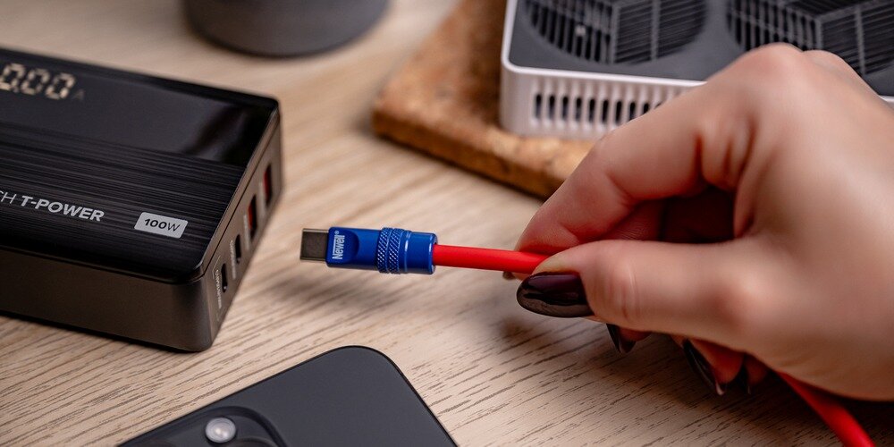 Kobieca dłoń wpina silikonowy kabel Newell USB-C do USB-C do leżącej na drewnianym blacie ładowarki.