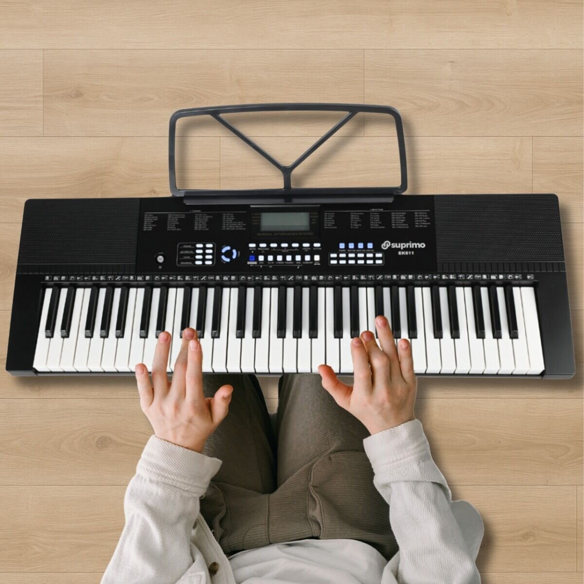 Osoba gra na elektronicznym keyboardzie z 61 klawiszami, na którym widoczne jest logo \'suprimo\'. Keyboard posiada pulpit do nut i różne przyciski funkcyjne na panelu sterowania.