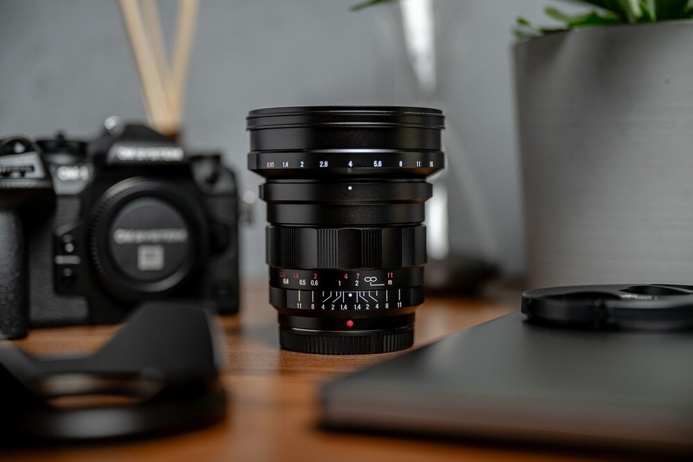 Obiektyw szerokokątny Nokton 10,5 mm f/0,95 MFT stoi na biurku w otoczeniu sprzętu foto-wideo przysłona f/0,95 jasność