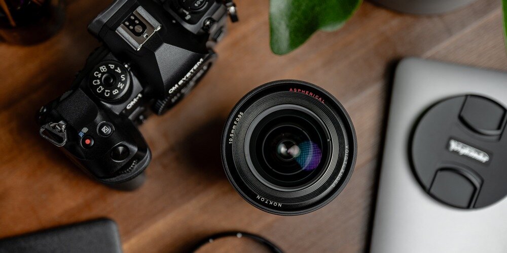 Obiektyw szerokokątny Nokton 10,5 mm f/0,95 MFT na biurku w otoczeniu sprzętu foto-wideo, ujęcie od góry Konstrukcja optyczna 13 soczewek ułożonych w 10 grupach