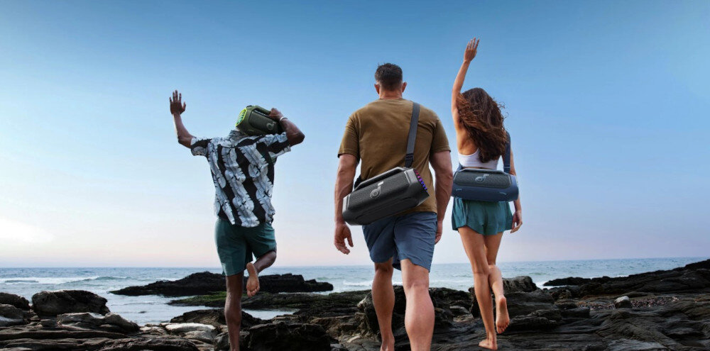 Głośnik mobilny SOUNDCORE Boom 2 Plus do słuchania muzyki w plenerze, osoby stojące na kamiennym podłożu z przewieszonymi na plecach głośnikami mobilnymi