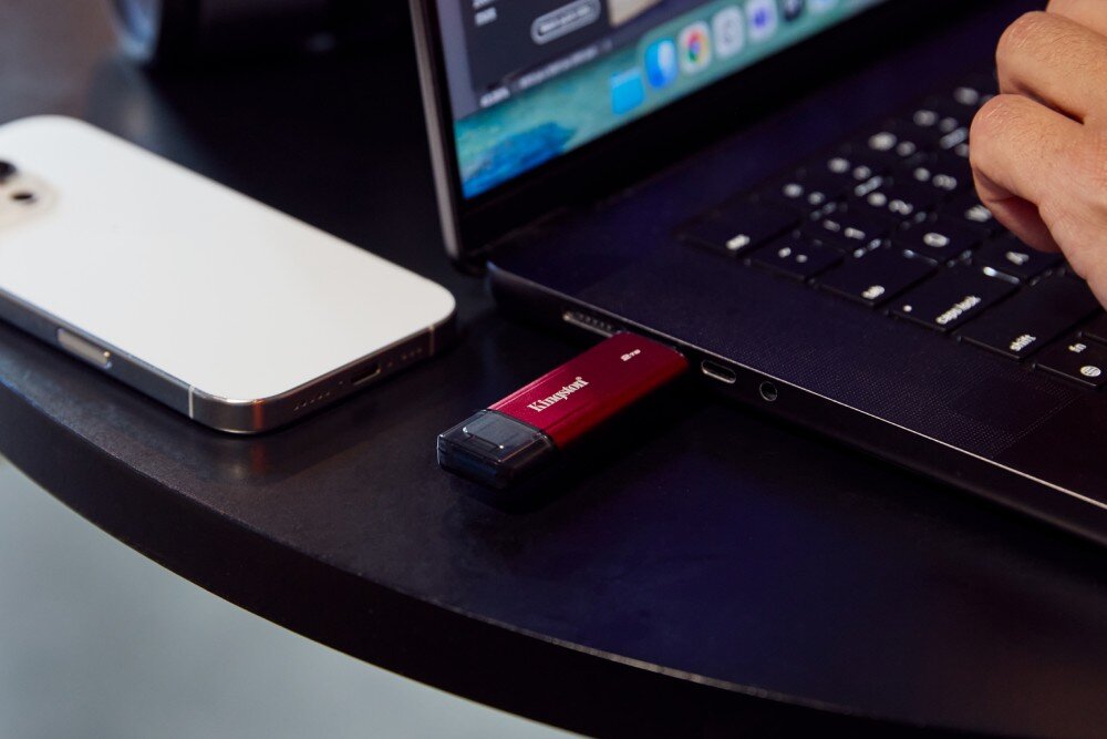 Dysk KINGSTON Dual Portable Małe, podłużne urządzenie jest wpięte do portu USB-C boku otwartego laptopa, obok którego leży smartfon, a na klawiaturze spoczywa dłoń, złącza, podłączenie
