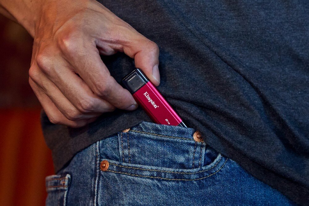 Dysk KINGSTON Dual Portable Małe, podłużne urządzenie jest wkładane przez dłoń do kieszeni zegarkowej pary niebieskich dżinsów, interfejs, prędkość
