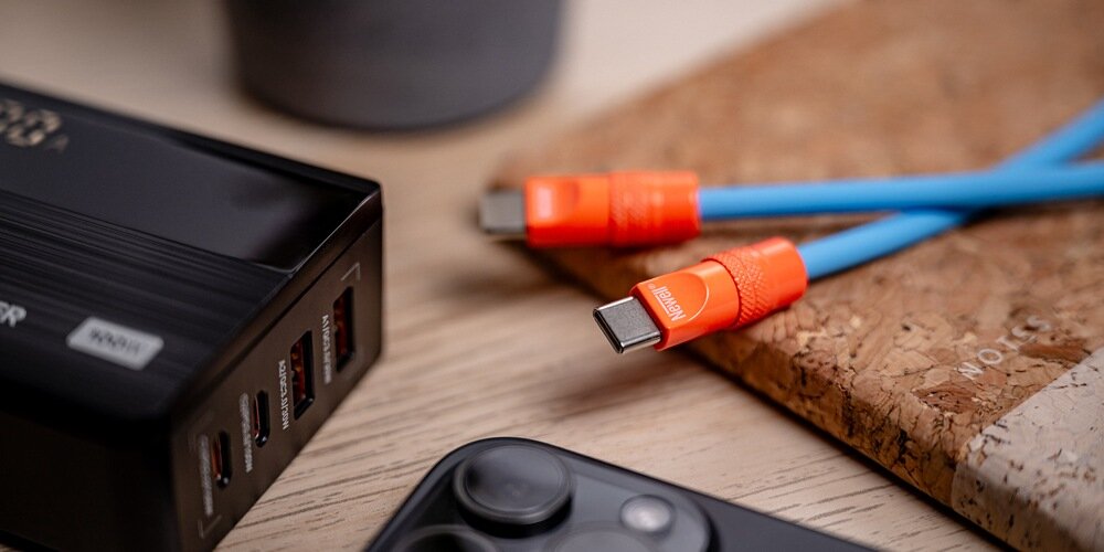 Na pierwszym planie czerwony, spiralny kabel Newell USB-C - USB-C 100 W. W tle rozmyte spiralne kable żółty i niebieski.