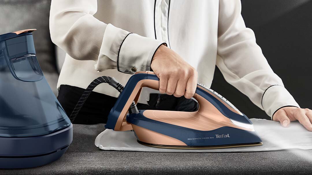 Kobieta prasuje białą tkaninę generatorem pary GV9910. Z przodu żelazka świeci się dioda LED.