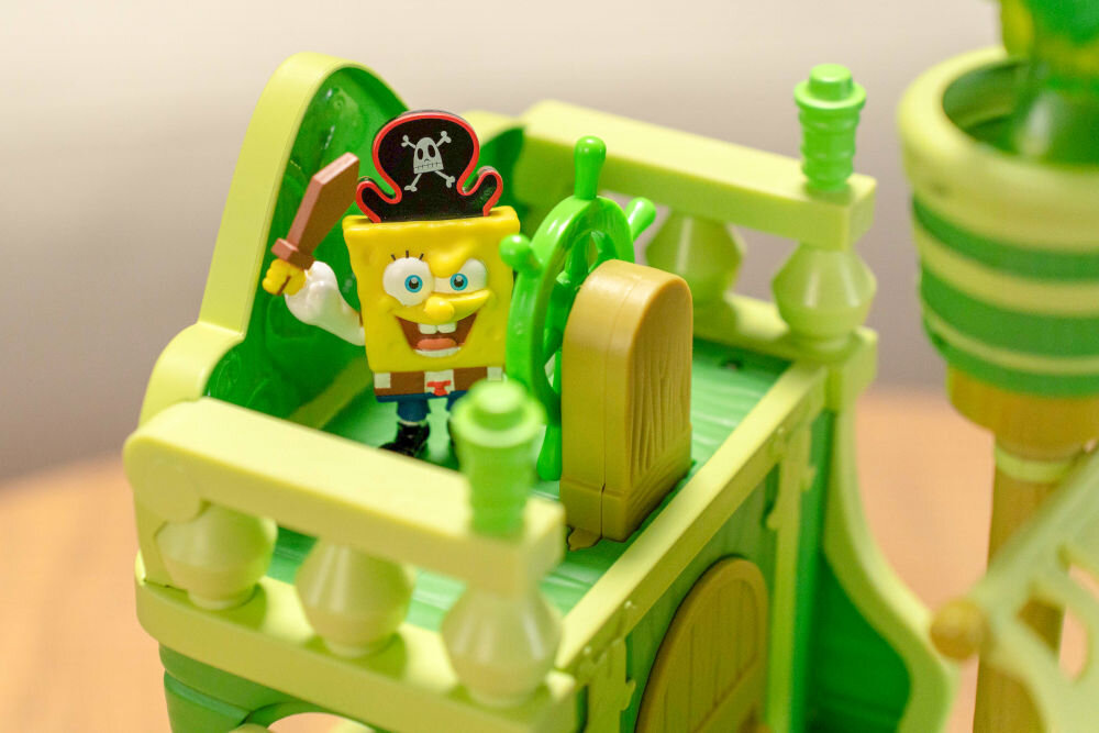 Zestaw figurek FUNRISE SpongeBob Latający Holender 73110 Zbliżenie na mostek kapitański zabawkowego statku Latający Holender. Figurka SpongeBoba w pirackim kapeluszu i z mieczem stoi przy zielonym sterze. Detale zabawki oddają klimat bajki SpongeBob Kanciastoporty.