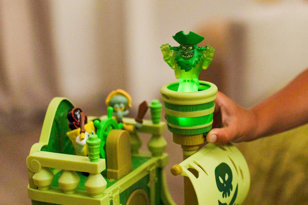 Zestaw figurek FUNRISE SpongeBob Latający Holender 73110 Zbliżenie na maszt zabawkowego statku pirackiego z serii SpongeBob. Widoczna dłoń aktywująca zielone podświetlenie w gnieździe wronim, które iluminuje przezroczystą figurkę ducha Latającego Holendra.