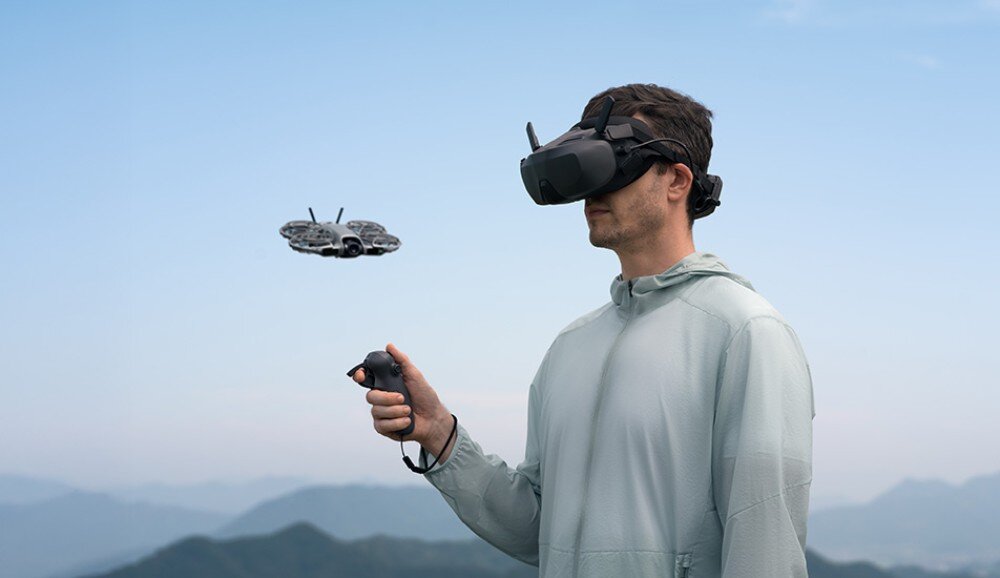 Dron DJI Neo 2 Fly More Combo Mężczyzna w goglach i z kontrolerem jednoręcznym steruje małym dronem na tle nieba, warianty, gogle