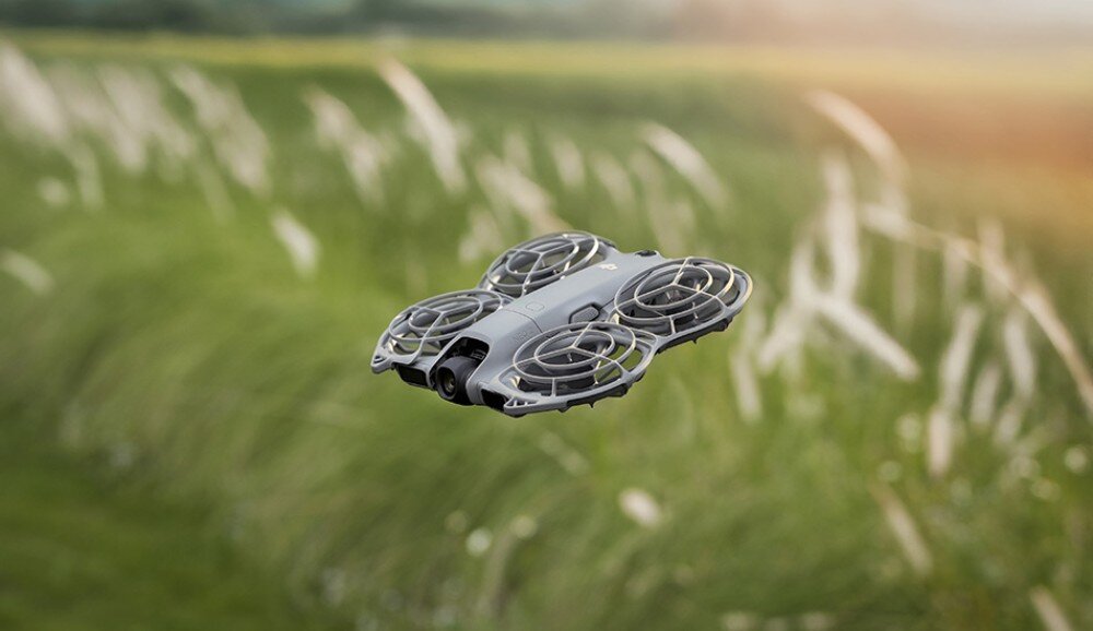 Dron DJI Neo 2 Fly More Combo Mały dron w locie nad zieloną łąką z rozmytym tłem traw, sensory, lot, osłony śmigieł