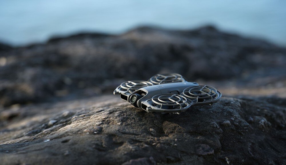 Dron DJI Neo 2 Fly More Combo Mały dron leży złożony na ciemnej skale przy wodzie, pamięć wewnętrzna, czas lotu, ładowanie