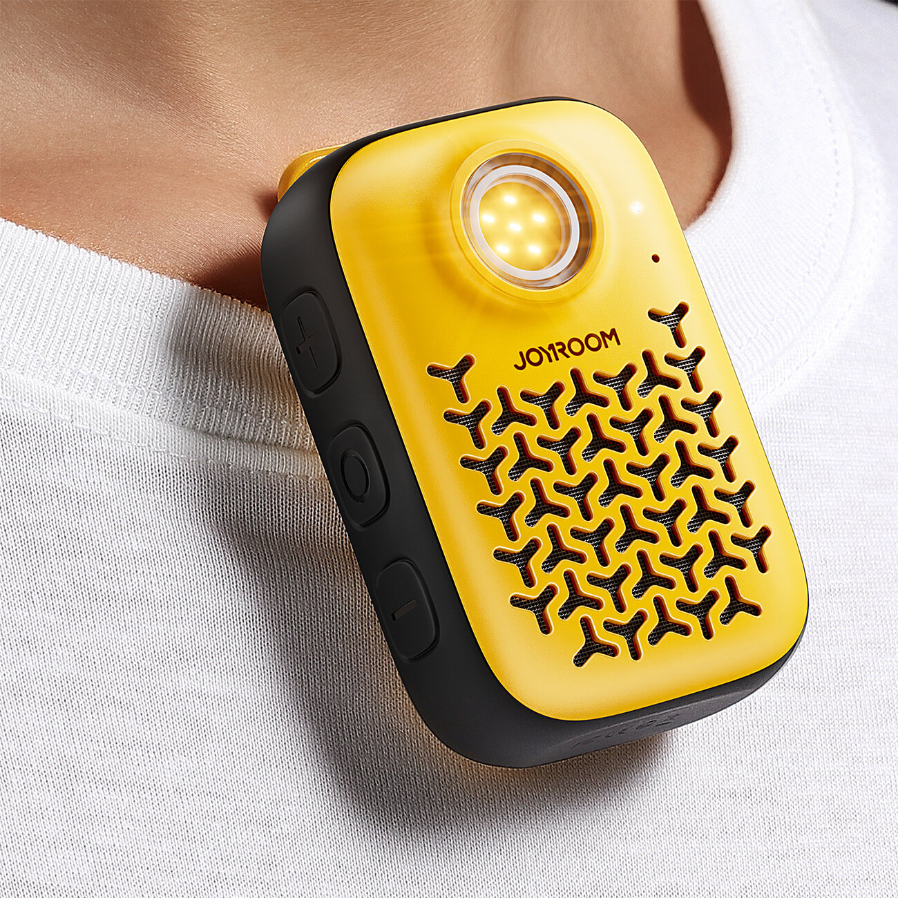 Żółty głośnik Bluetooth z wbudowaną latarką, z widocznym logo \'JOYROOM\', przymocowany do białej koszulki. Na obudowie znajdują się przyciski oraz otwory w kształcie litery Y.