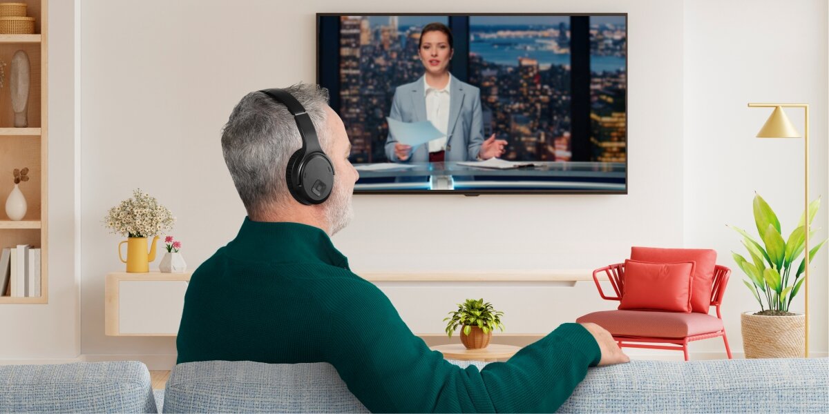 Słuchawki powietrzne HAMA Telewizyjne Piaskowy Starszy mężczyzna w czarnych słuchawkach bezprzewodowych Hama ogląda wiadomości w jasnym salonie.