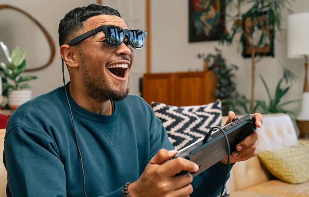 Okulary VITURE XR Luma Pro Czarny mężczyzna grający na konsoli w pokoju na kanapie z założonymi okularami platforma SpaceWalker konfiguracja własnego wieloekranowego środowiska Android iOS Windows macOS magnetometr niwelacja przesunięcia obrazu technologia konwersji 2D na 3D w czasie rzeczywistym