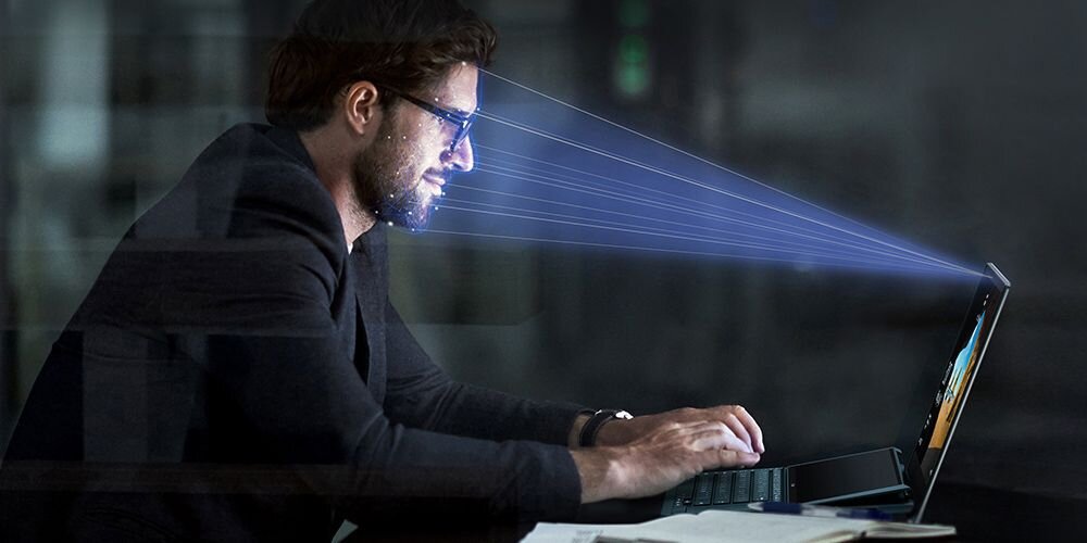 Mężczyzna w okularach używający laptopa ASUS ZenBook z wizualizacją niebieskich linii kamery IR do rozpoznawania twarzy w ciemnym otoczeniu biurowym - Kamera IR z Windows Hello 