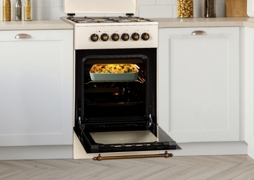 Kuchnia gazowo-elektryczna w zabudowie kuchennej z otwartym piekarnikiem. W środku piekarnika zapiekanka.
