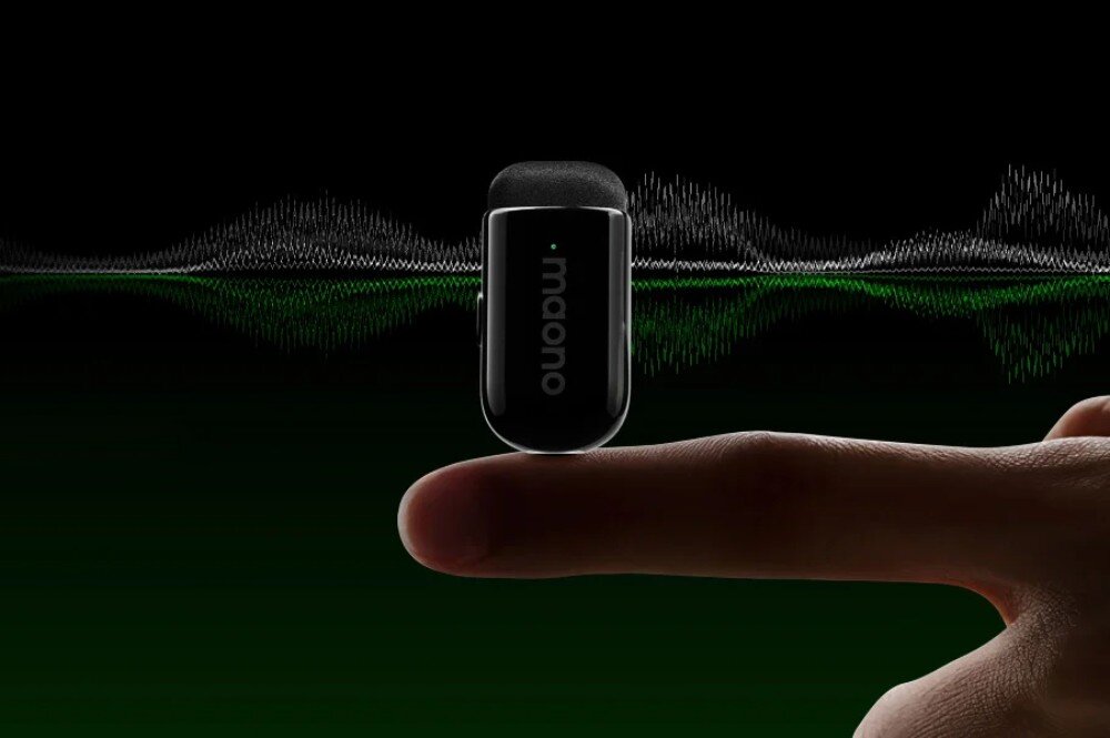 System bezprzewodowy MAONO WM622 PC2 czarny, błyszczący mikrofon o obłym kształcie umieszczony na czubku palca wskazującego, w tle widoczna jest graficzna wizualizacja fali dźwiękowej w kolorach białym i zielonym na czarnym tle