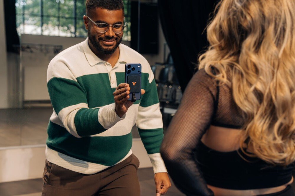 Dysk VERBATIM SnapBack Ultra Slim Mężczyzna w swetrze w pasy nagrywa smartfonem kobietę z długimi blond włosami, trzymając urządzenie pionowo z widocznym akcesorium pamięci na pleckach telefonu, zasilanie, oprogramowanie