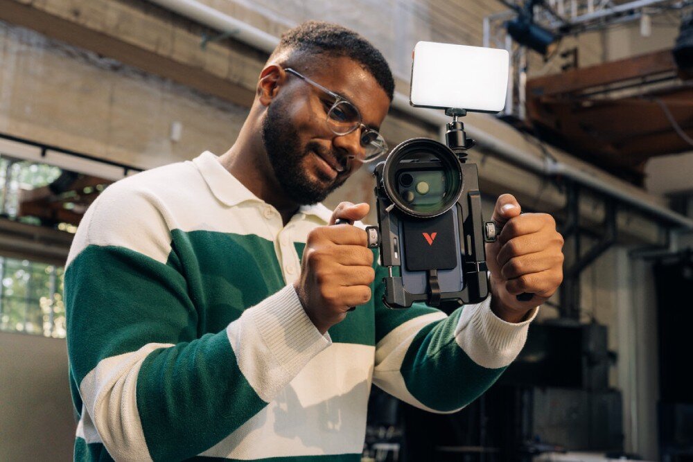 Dysk VERBATIM SnapBack Ultra Slim Mężczyzna trzyma w dłoniach smartfon umieszczony w profesjonalnej klatce operatorskiej z dołączonym oświetleniem, zewnętrznym obiektywem i dyskiem zamontowanym na tylnej obudowie, interfejs, przepustowość, prędkość