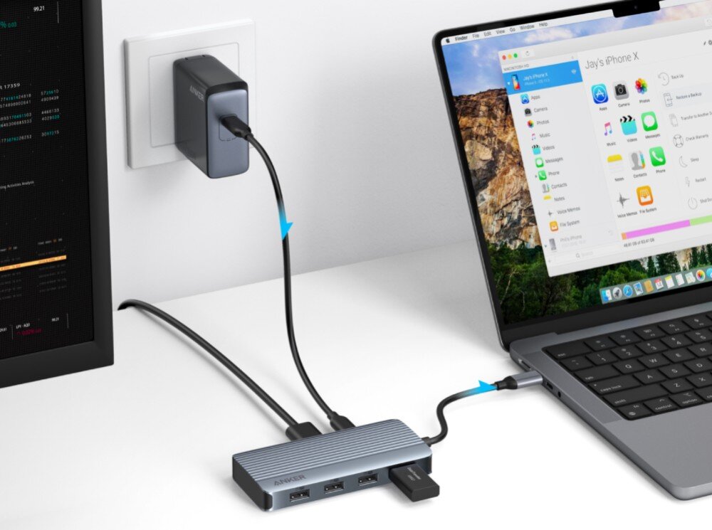 Hub ANKER A83740A2 7w1 Ilustracja pokazująca przepływ energii od ładowarki ściennej przez kabel USB-C do adaptera, a następnie do laptopa, z widocznym w tle monitorem i podłączoną pamięcią przenośną