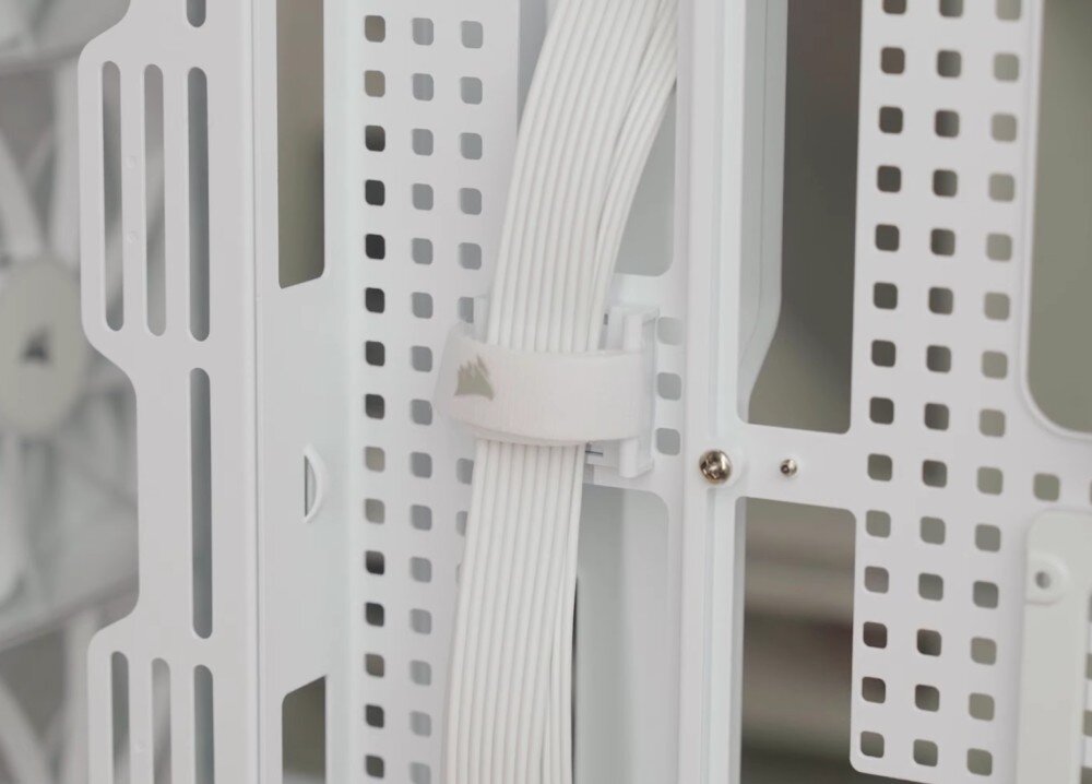 Obudowa CORSAIR Frame 5000D RS ARGB Widok na tył tacki płyty głównej z systemem zarządzania okablowaniem. Wiązka przewodów w oplocie jest uporządkowana i przytrzymywana przez materiałowy rzep z logo producenta, przechodząc przez otwory w konstrukcji