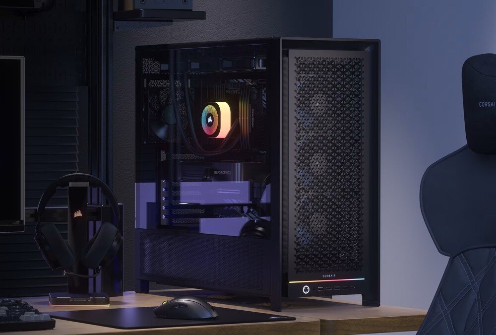 Obudowa CORSAIR Frame 5000D RS Komputer stacjonarny w czarnej obudowie z przeszklonym panelem bocznym, przez który widać podświetlone na kolorowo komponenty, umieszczony na biurku obok słuchawek i myszki