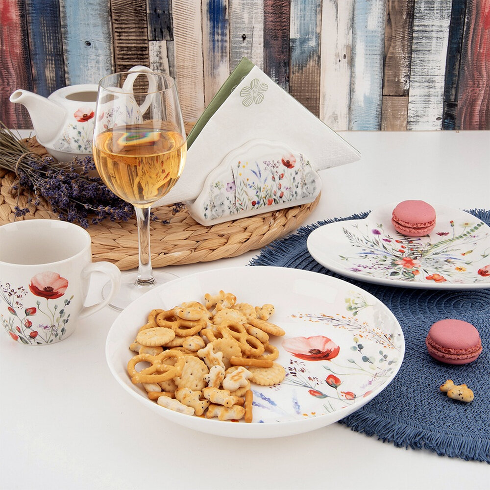 Na stole znajduje się porcelanowy talerz z motywem kwiatowym, wypełniony przekąskami. Obok widoczne są filiżanka, dzbanek, kieliszek z napojem oraz serwetnik, wszystkie z podobnym wzorem kwiatowym.