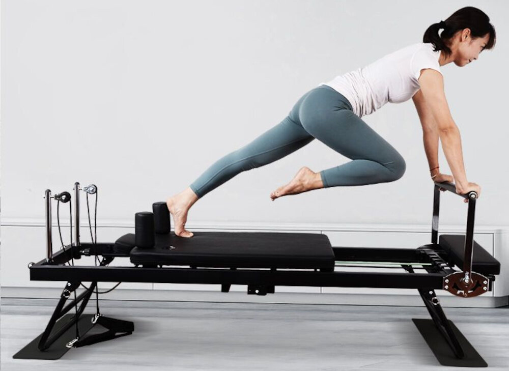 Reformer do pilatesu EXTRALINK Lifestyle PB1001 Czarny pokój osoba ćwiczy na reformerze ze stali nierdzewnej odporność na uszkodzenia i stabilność obciążenie do 120 kg precyzja ruchów komfort użytkowania długa żywotność