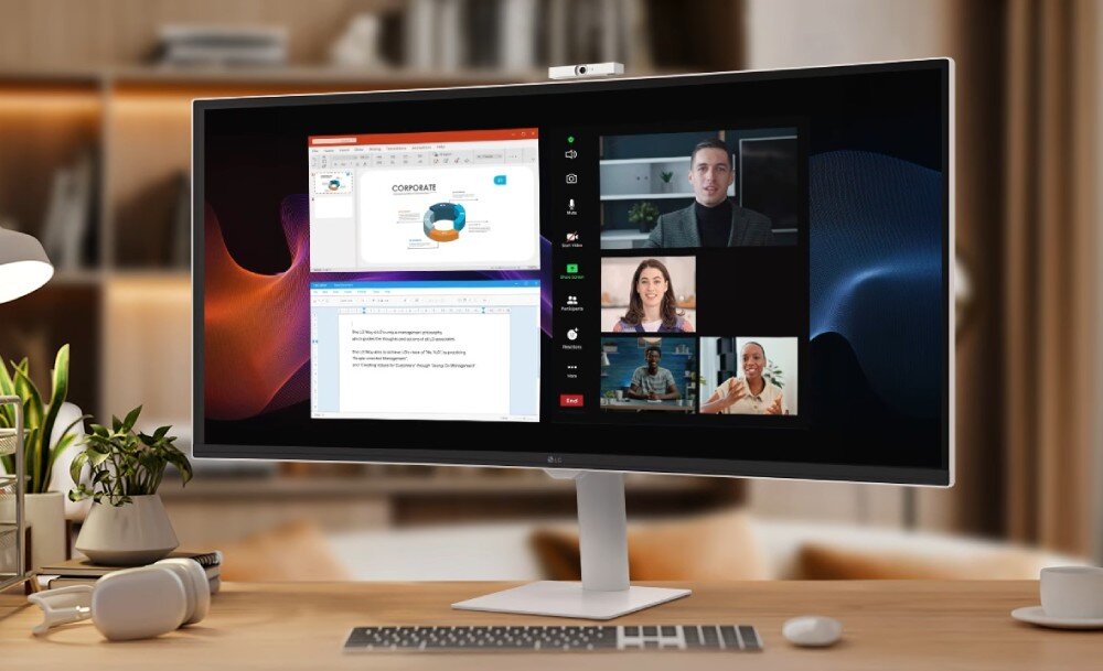 Monitor wyświetla podzielony ekran z prezentacją i wideokonferencją z kilkoma osobami. Na biurku przed monitorem znajdują się słuchawki i klawiatura.