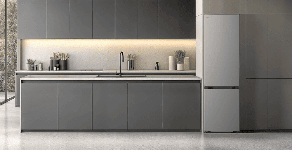 LODÓWKA LG GBBSJ2CCPY Minimalistyczna kuchnia w odcieniach grafitu z długą wyspą i gładkimi frontami bez uchwytów, podświetlana ciepłą listwą LED, z ciemną lodówką wolnostojącą wkomponowaną w zabudowę po prawej stronie