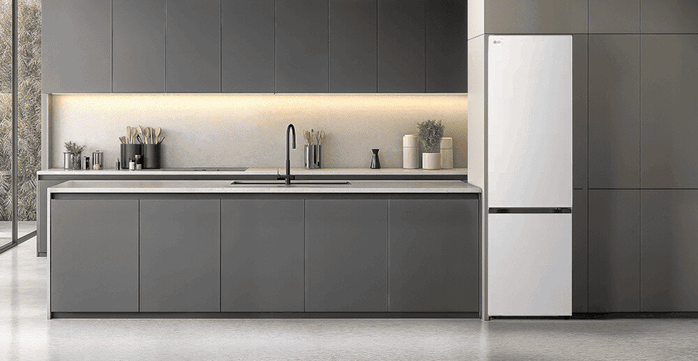 LODÓWKA LG GBBSJ20ESW Minimalistyczna kuchnia w odcieniach grafitu z długą wyspą i gładkimi frontami bez uchwytów, podświetlana ciepłą listwą LED, z ciemną lodówką wolnostojącą wkomponowaną w zabudowę po prawej stronie
