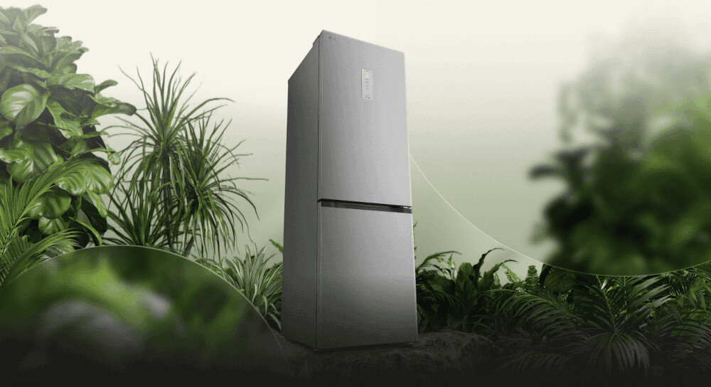 LODÓWKA LG GBBSJ11EPY Grafika przedstawia smukłą, ciemnoszarą lodówkę LG ustawioną pośród bujnej, zielonej roślinności na tle jasnego, rozmytego nieba. Kompozycja podkreśla ekologiczny charakter urządzenia, kojarząc je z naturą i energooszczędnością energooszczędna efektywma praca klasa C