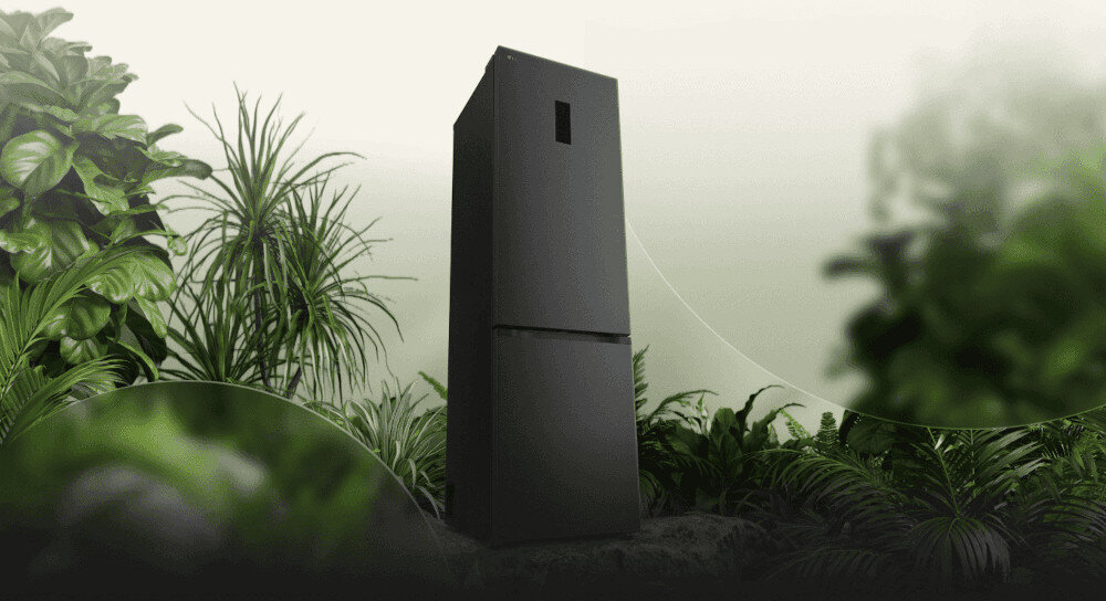 LODÓWKA LG GBBS727AEV Grafika przedstawia smukłą, ciemnoszarą lodówkę LG ustawioną pośród bujnej, zielonej roślinności na tle jasnego, rozmytego nieba. Kompozycja podkreśla ekologiczny charakter urządzenia, kojarząc je z naturą i energooszczędnością energooszczędna efektywma praca klasa A