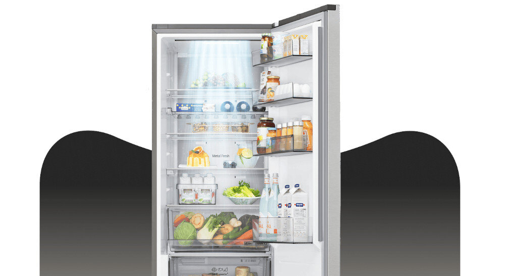 LODÓWKA LG GBBS525CPY Grafika przedstawia otwartą lodówkę LG z górną chłodziarką, wypełnioną jedzeniem rozmieszczonym na półkach, w szufladach i na balkonikach drzwi. Jasne oświetlenie LED w górnej części komory równomiernie rozjaśnia wnętrze, eksponując świeże warzywa, owoce, napoje oraz produkty w opakowaniach kartonowych i słoikach DoorCooling+ LG szybkie chłodzenie równomierne chłodzenie chłodzenie drzwi świeżość żywności chłodne napoje technologia LG lepsza cyrkulacja powietrza dłuższa świeżość