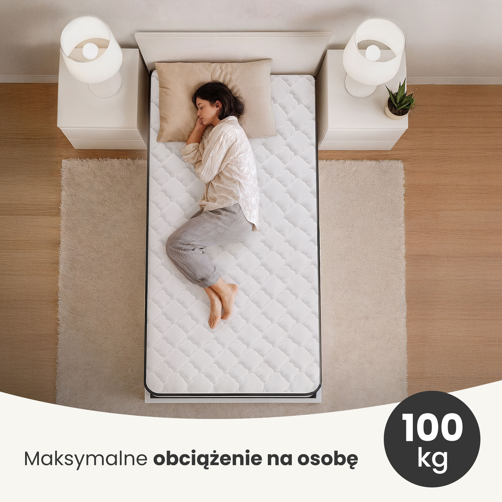 Osoba leży na białym materacu sprężynowym z ochraniaczem, umieszczonym na łóżku pomiędzy dwoma stolikami nocnymi z lampkami. Na dole obrazu widnieje napis: \'Maksymalne obciążenie na osobę 100 kg\'.