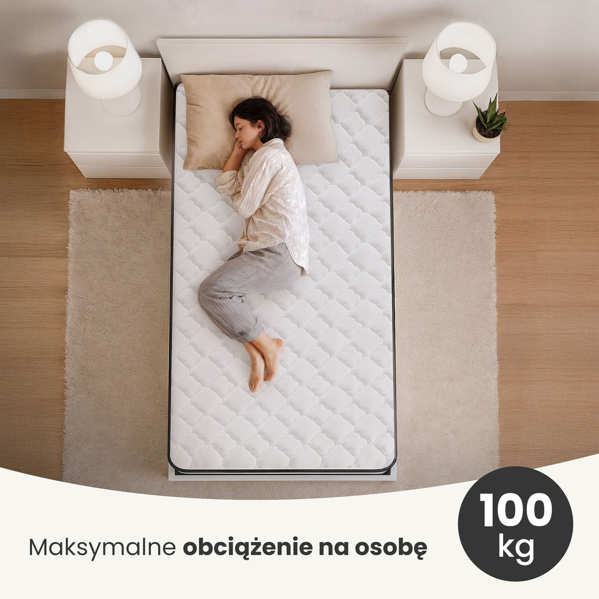 Osoba leży na białym materacu sprężynowym w pokoju z dwoma stolikami nocnymi i lampkami. Tekst na obrazie: \'Maksymalne obciążenie na osobę 100 kg\'.