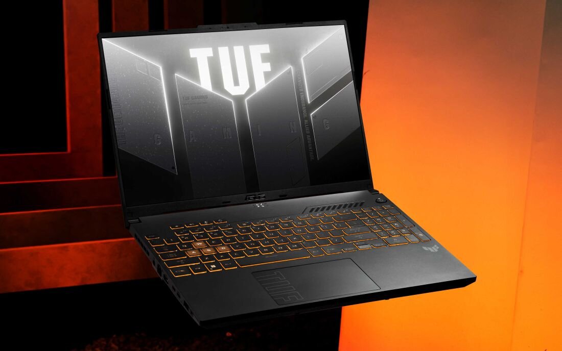 ASUS TUF Gaming F16 na pomarańczowym tle z czerwonymi elementami i logo TUF na ekranie z podświetloną klawiaturą RGB, prezentującym łączność Wi-Fi 6E 802.11ax z prędkościami do 2.4 Gbps, pasmo 6GHz bez interferenci i stabilnym połączeniem dla gamingu online bez opóźnień - Wi-Fi 6 Bluetooth 5.2 