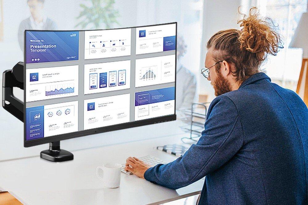 Uchwyt do monitora REDRAGON GMK914 Mężczyzna siedzi tyłem przy biurku i patrzy na szeroki, zakrzywiony monitor wyświetlający prezentację, który jest zamontowany na czarnym uchwycie biurkowym