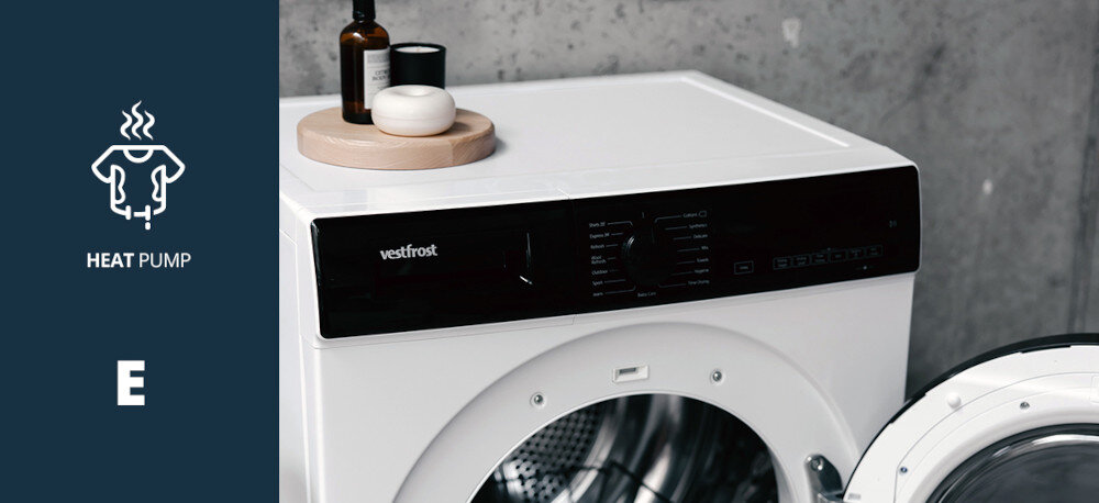 Suszarka VESTFROST VT-FW4EHY70EU Na zdjęciu pokazano fragment panelu sterującego suszarki marki Vestfrost, uchwycony z bliska w wnętrzu. Po lewej stronie widnieje grafika informująca o technologii pompy ciepła Heat Pump oraz klasie energetycznej E pompa ciepła energooszczędna niskotemperaturowa klasa energetyczna E ochrona tkanin delikatne suszenie oszczędna Vestfrost pompa ciepła